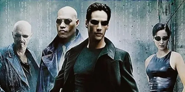 A poster for the film The Matrix. There are 4 people stood in a row, cut from different scenes, wearing black with dark sunglasses.