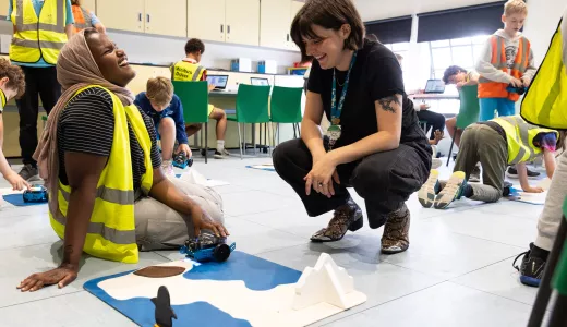 A member of staff and school pupil sat on the floor in a classroom environment. They are both laughing together next to a model of an arctic environment