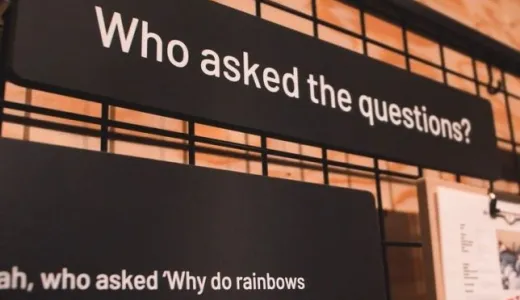 Black signage with white writing reading 'who asked the questions?' 