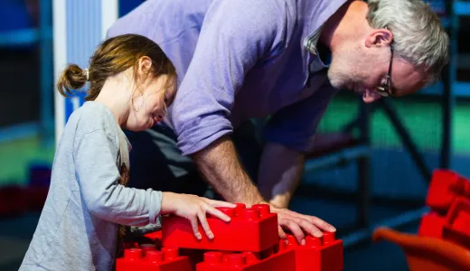 An adult and child working together with large red building bricks