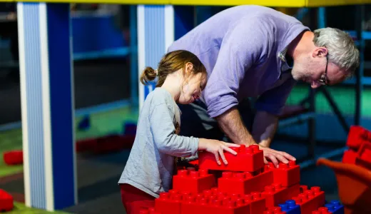 An adult and child working together with giant red building bricks