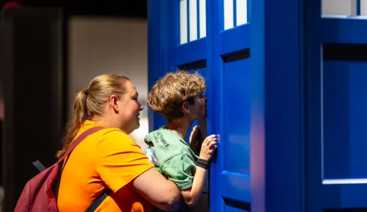 An adult is lifting up a child to peer into the TARDIS in a science centre.