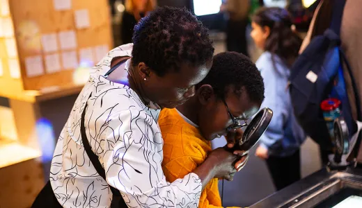 A person holding a magnifying glass helping a child explore and exhibit together in an interactive science centre. 