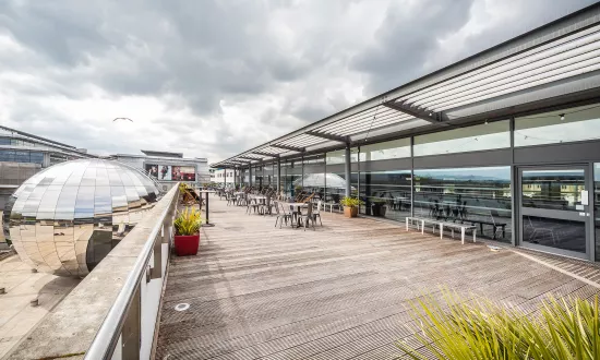 A large terrace with wooden decking overlooking Millennium Square. A big silver mirrored ball; The Planetarium can be seen in the background