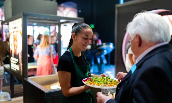 A waitress handing out a plate full of canapés to a man in the We The Curious venue