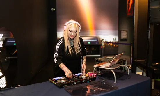 A woman wearing headphones performing behind a DJ mixing table in the We The Curious venue