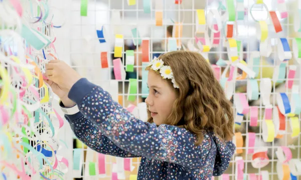 A child putting a colourful ribbon on a wall full of colourful ribbons