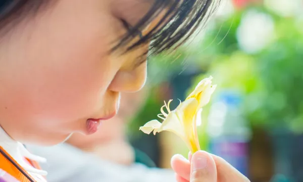 A child with headphones blowing air into a flower 