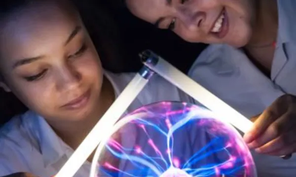 Two children holding small light tubes a Plasma ball is between them and this is causing the light tubes to illuminate.