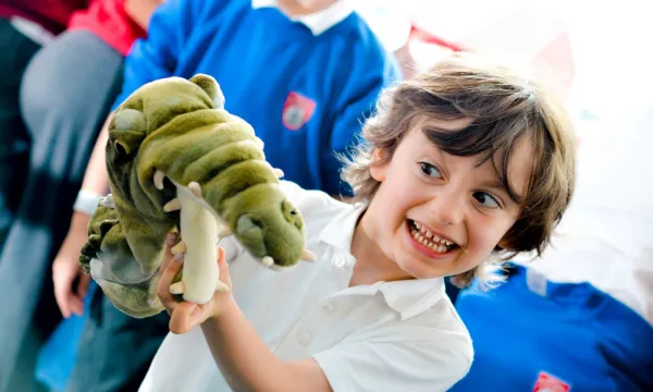 A child smiling and playing with a crocodile puppet 