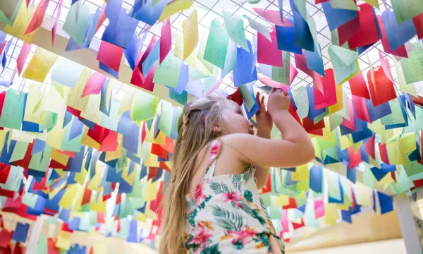 A child peering at colourful tags hanging from the ceiling of the question cube