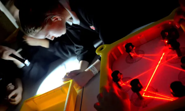 a child looking at a bright light on a table, with an exhibit with red lasers next to them