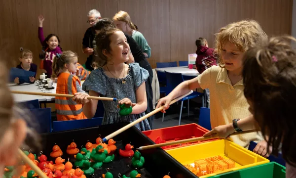 children hooking orange and green ducks, with more people in the background