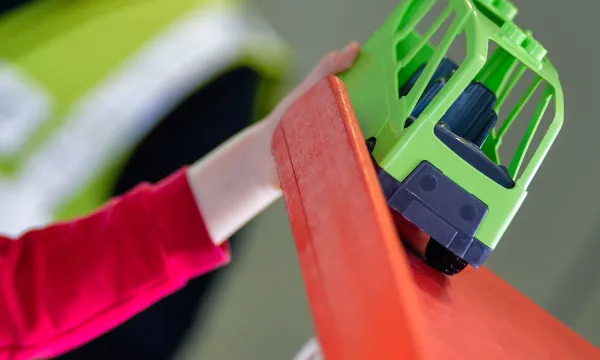 a hand holding a green truck at the top of a red ramp