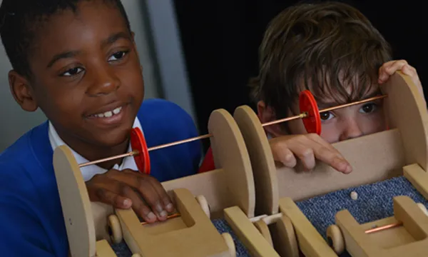 2 children are releasing wooden cars down a carpet covered ramp