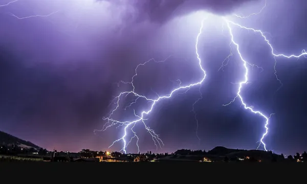 a dark sky with multiple lightning flashes, above buildings with lights on