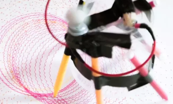 a bot made of a circuit, cup, and pens scribbling circles on paper