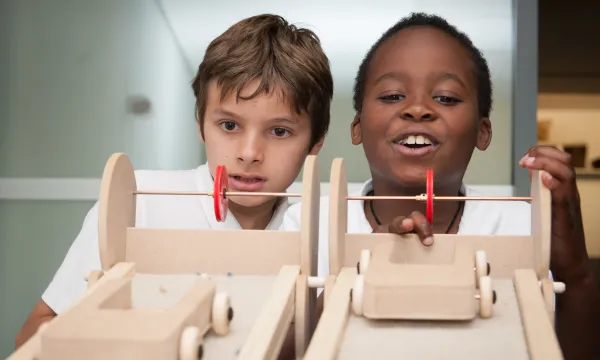 Two children looking amused and concentrated whilst playing with a wooden race car structure in an education workshop  