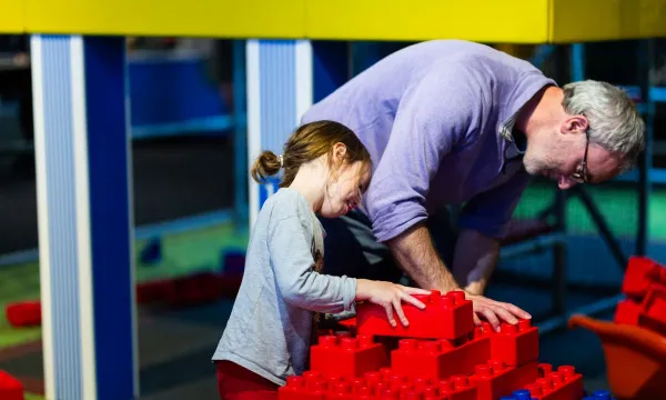 A person and a child making something out of giant red lego blocks