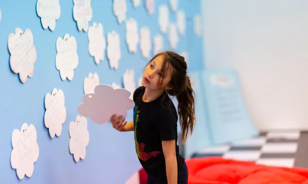 A child looking contemplatively at a wall full of self care ideas written on cloads 