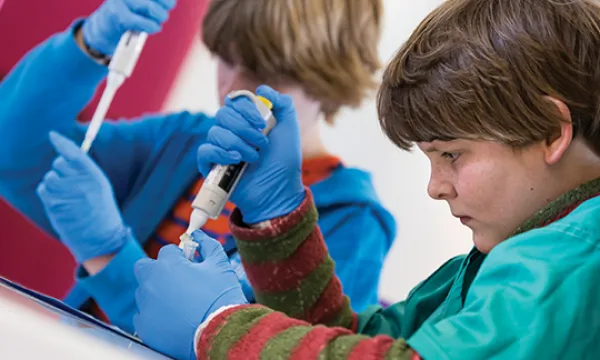 Two students wearing blue gloves practice pipetting