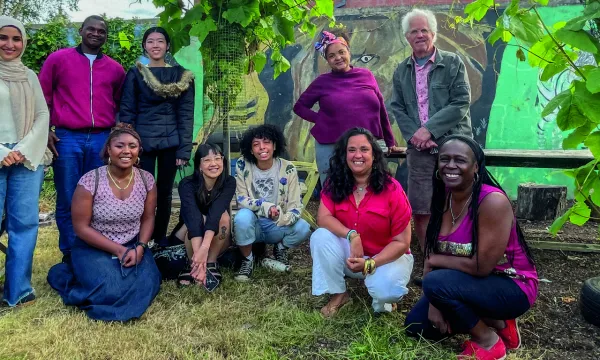 A group of people in front of some plants, together for a photo. Some are crouched, some are stood up.