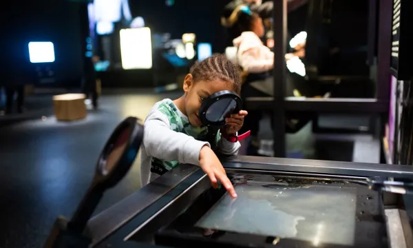 A child looking at water through a magnify glass