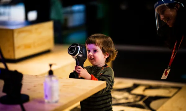 A small child is in the middle of a wooden space holding up a camera device.