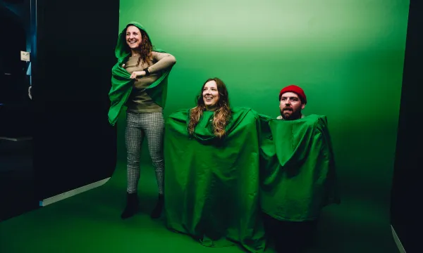 A group of people are in front of a green screen covering their bodies with green cloaks.