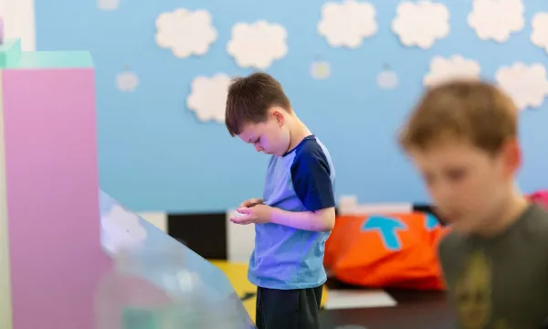 A child in front a wall full of cloud inquisitively looking at something in their hands