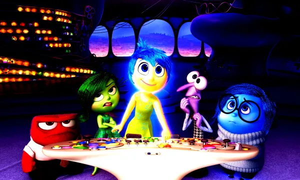 Promotion picture for the animated film Inside Out featuring the main character Ryle standing behind a table surrounded by animated figures representing her emotions 