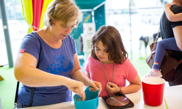 An adult and child are together in a kitchen space with a brightly coloured bowl on a white surface. 
