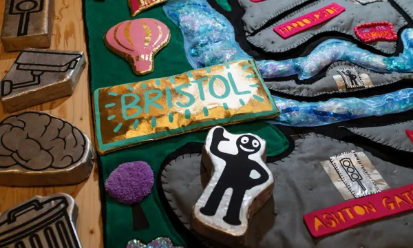 A colourful handcrafted collage with raised icons, including a “BRISTOL” sign, a hot air balloon, a waving Morph figure arranged on a textured map-like background