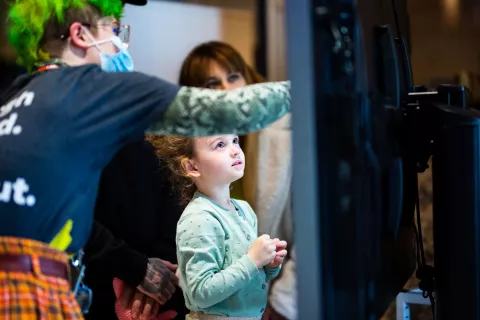 A young child is looking up at a digital screen, which a We The Curious member staff is pointing to 