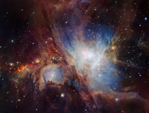 The Orion Nebula. A black background with clouds of blue, red and white, and some stars.