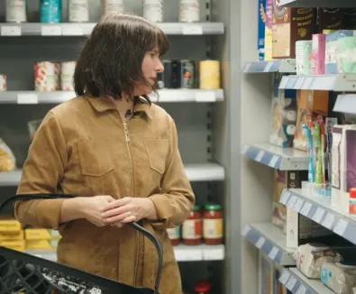 A person in a supermarket, carrying a shopping basket and looking at items.