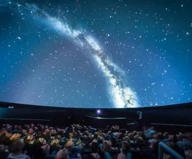 Inside of a planetarium.  The room is full of people looking up at a dome showing the edge of the galaxy.