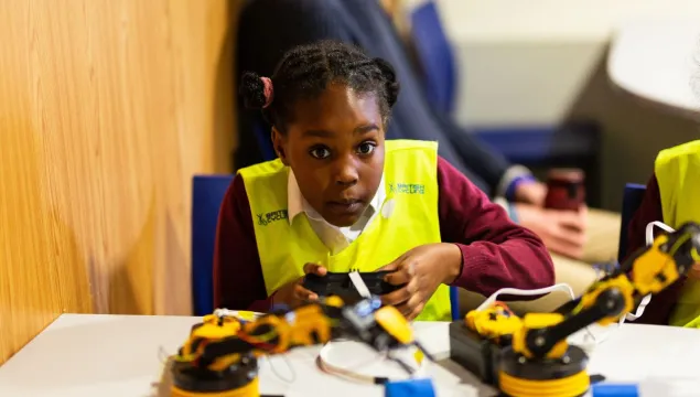 A kid in a high-vis looking really excited about playing with robots in front of them