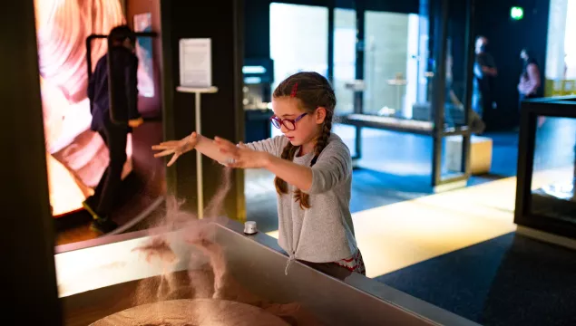 A child playing with the sand exhibit in We The Curious