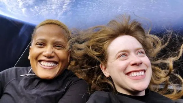 Two female astronauts in space with the Earth behind them.  They are both smiling a lot.