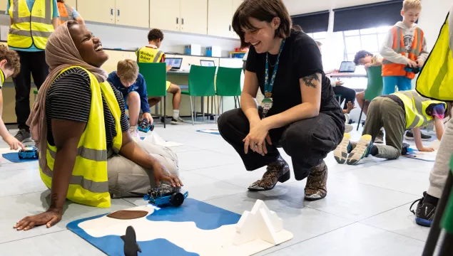 A member of staff and school pupil sat on the floor in a classroom environment. They are both laughing together next to a model of an arctic environment