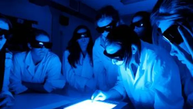 A group of students in lab coats looking at a light box in a dark room