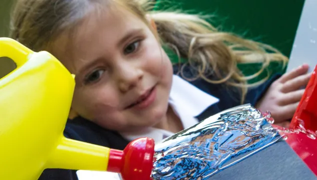 a child with bunches watches water being poured on a roof tile with a yellow and red watering can