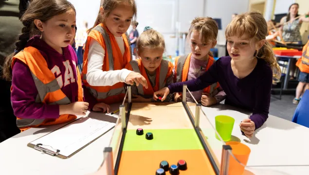 a group of children rolling pucks along a board with green, orange, and red sections