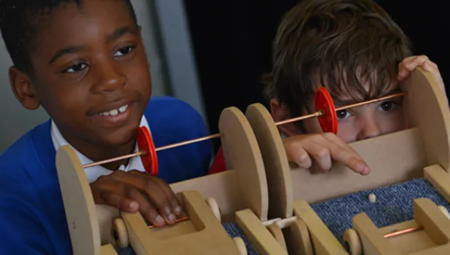 2 children are releasing wooden cars down a carpet covered ramp