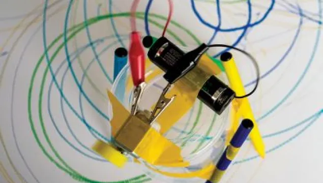 a top down view of a bot made of a circuit, cup, and pens on a scribble that it has created