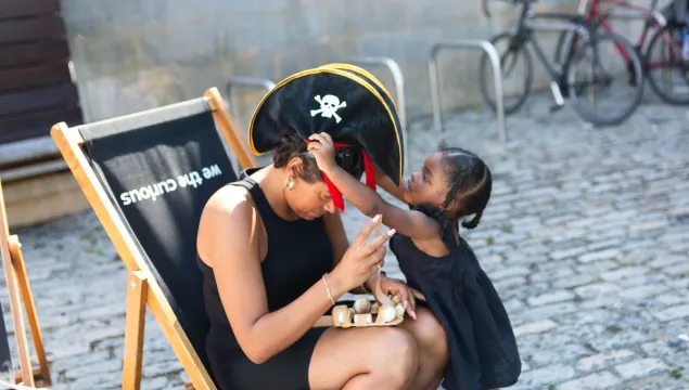 A small child putting a pirate hat on a person sitting in a deck chair