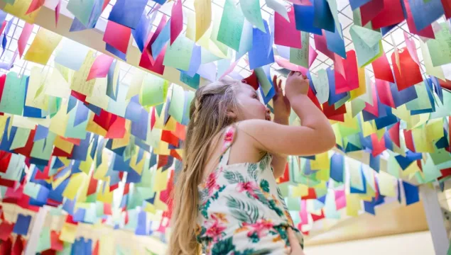 A child being lifted high up to be able to look at colourful tags filled with questions