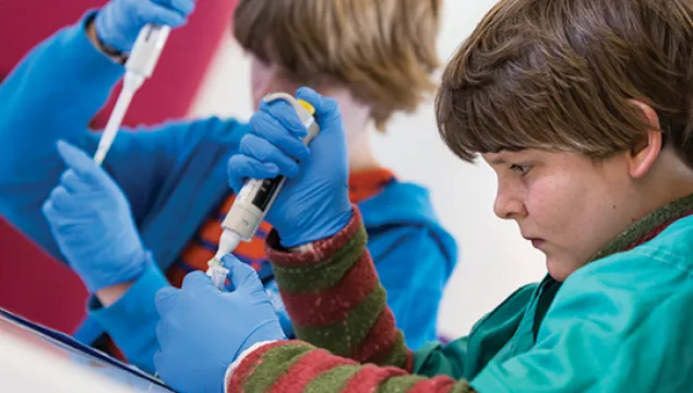 Two students wearing blue gloves practice pipetting