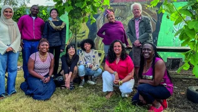 A group of people in front of some plants, together for a photo. Some are crouched, some are stood up.